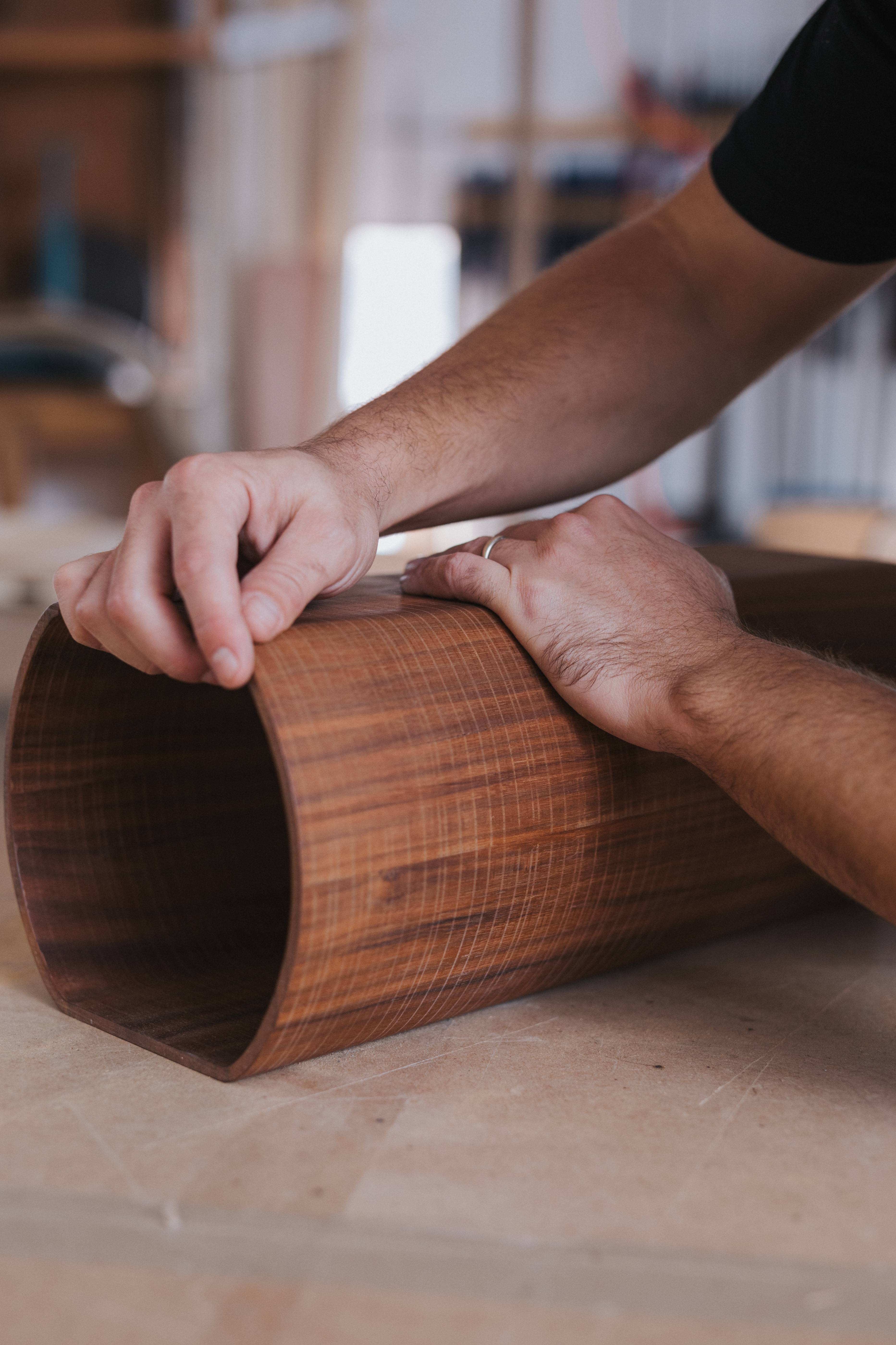 Two hands pressing a sheet of walnut veneer into a curved form.