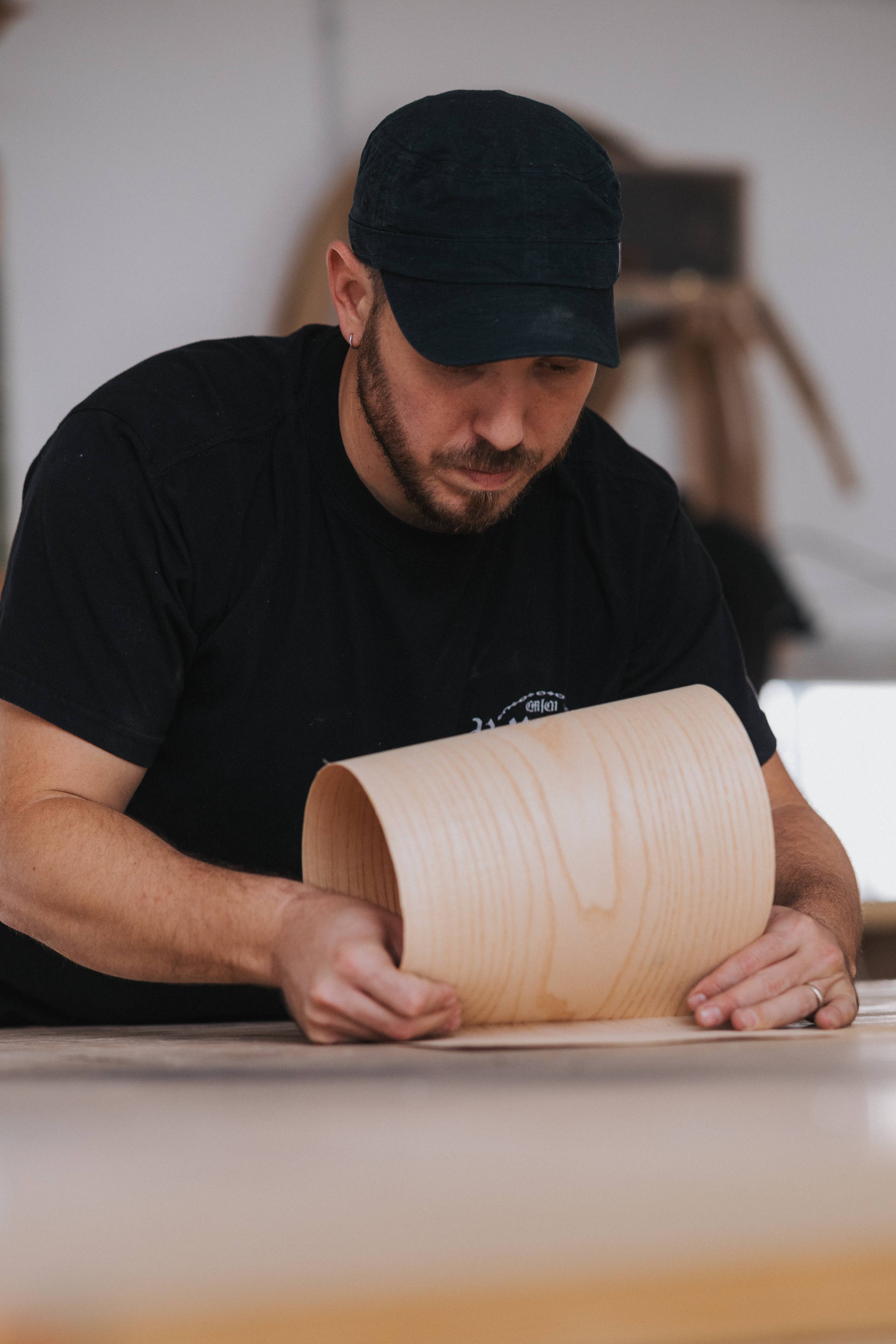 Shay Hoffenbartel at the workbench, bending a sheet of pale wood veneer.
